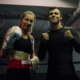 Twee lachende boksers, een vrouw met witte bokshandschoenen en een man in zwarte sportkleding poseren vriendschappelijk samen in de boksring na een training bij Boxing University Breda.